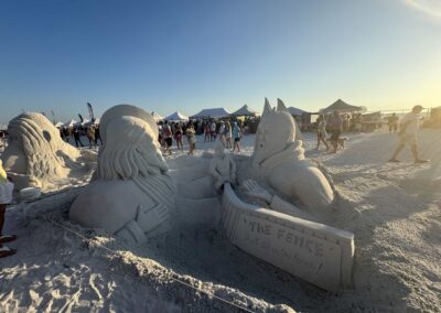 Two sand figures divided by a fence sculpture with the message “Don’t sit on the fence!”