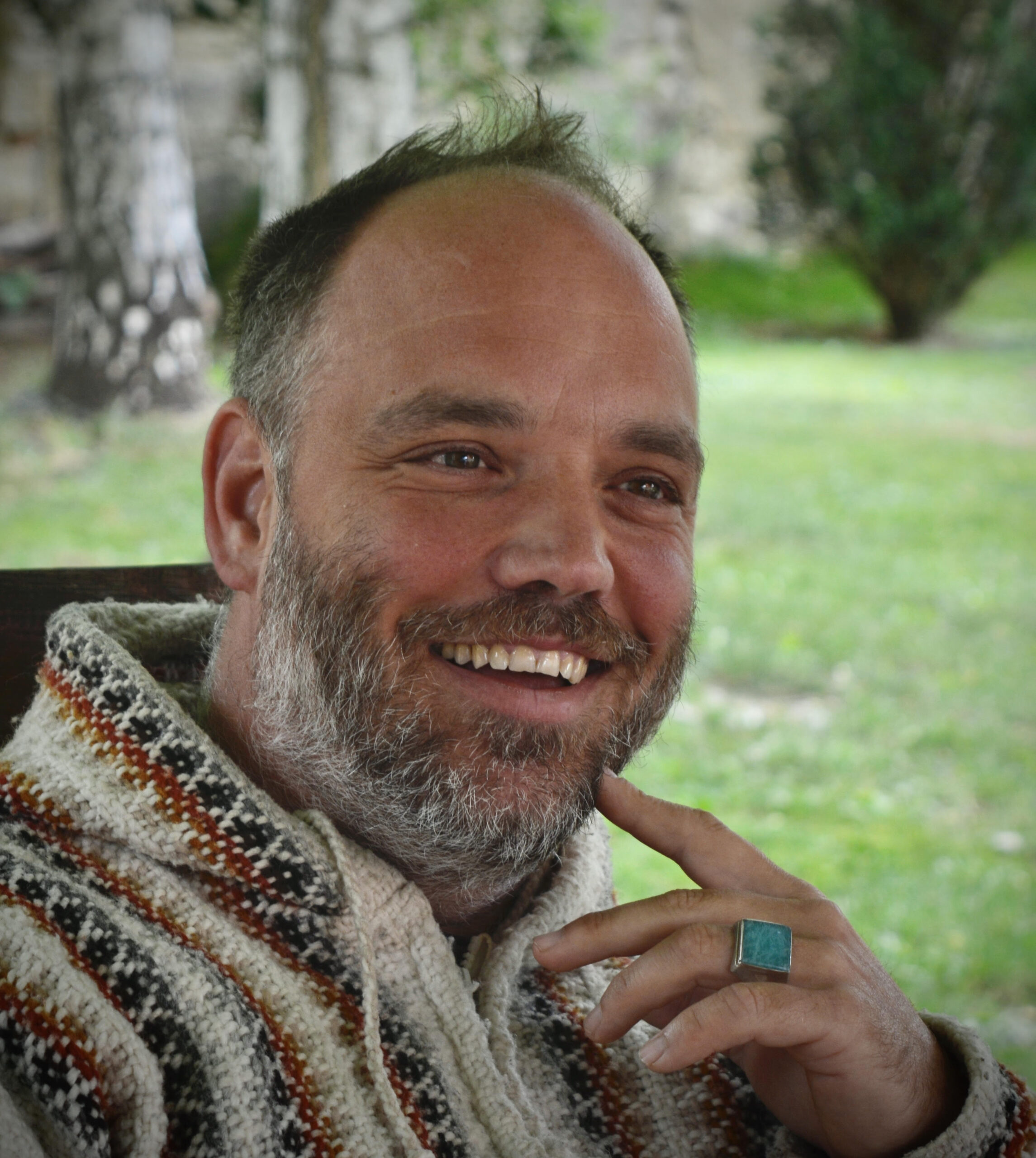 Person in striped sweater smiles outdoors, hand near chin with turquoise ring.